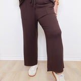 Person wearing brown pants and white sneakers against a white wall.