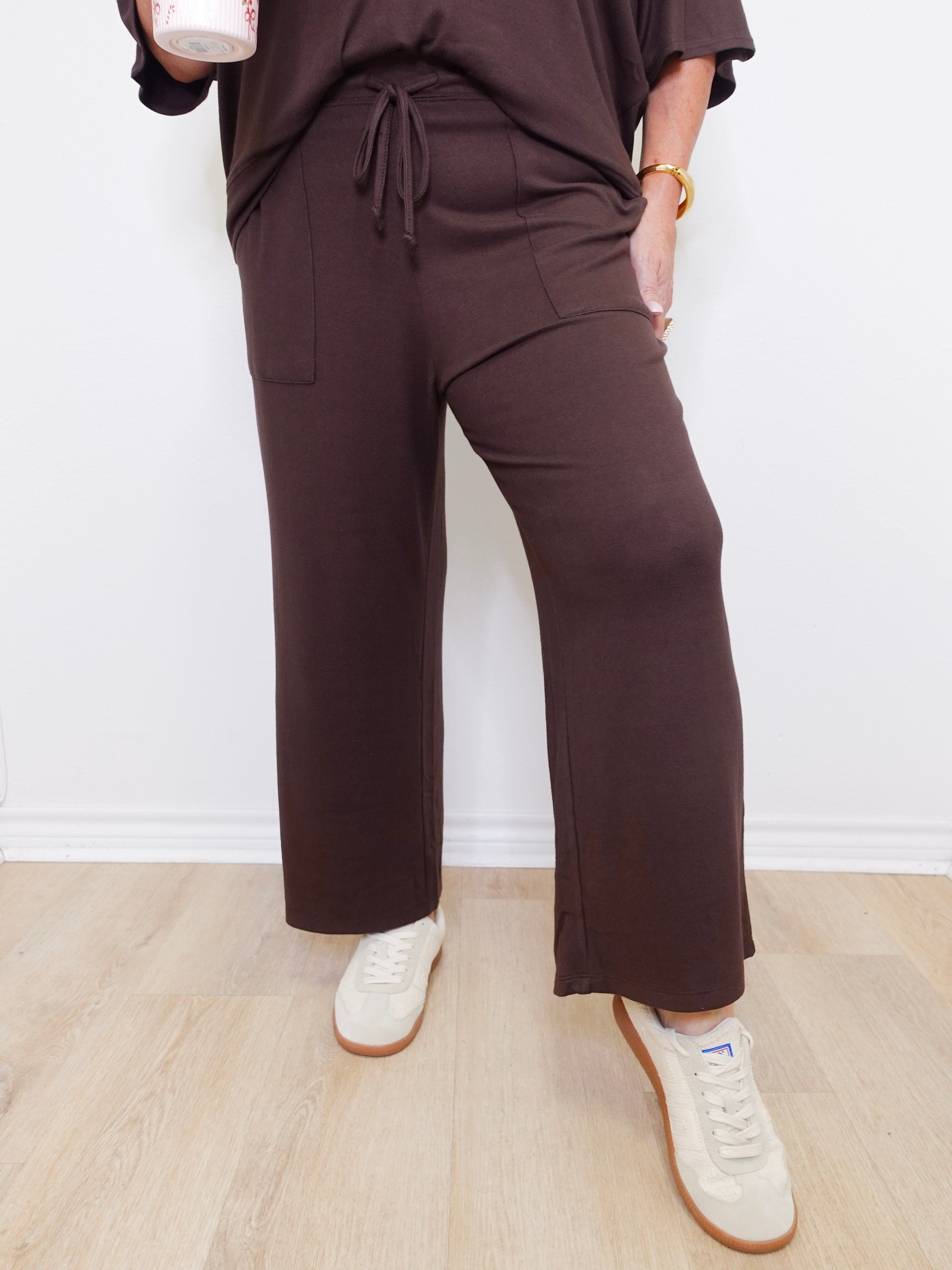 Person wearing brown pants and white sneakers against a white wall.