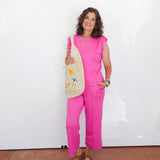 Woman in a pink outfit holding a straw bag with a white background