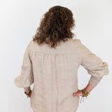 Person wearing a beige blouse with long sleeves on a white background