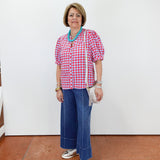 Woman wearing a red checkered shirt and blue pants against a white wall.