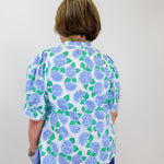 Person wearing a floral blouse with blue and green flowers on a plain background