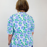 Person wearing a floral blouse with blue and green flowers on a plain background