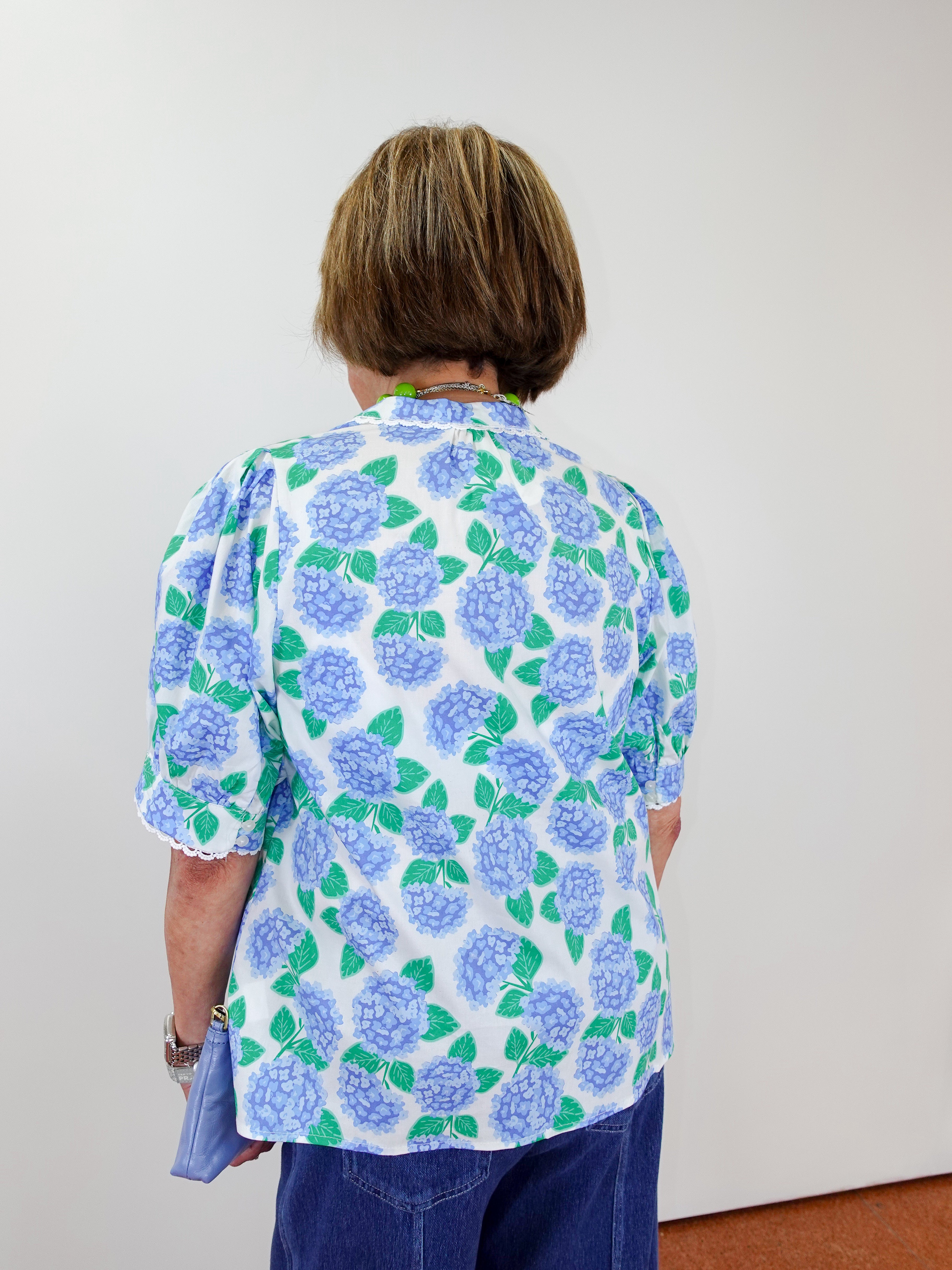Person wearing a floral blouse with blue and green flowers on a plain background