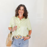 Woman wearing a light green shirt and blue jeans, holding a beige handbag against a white background