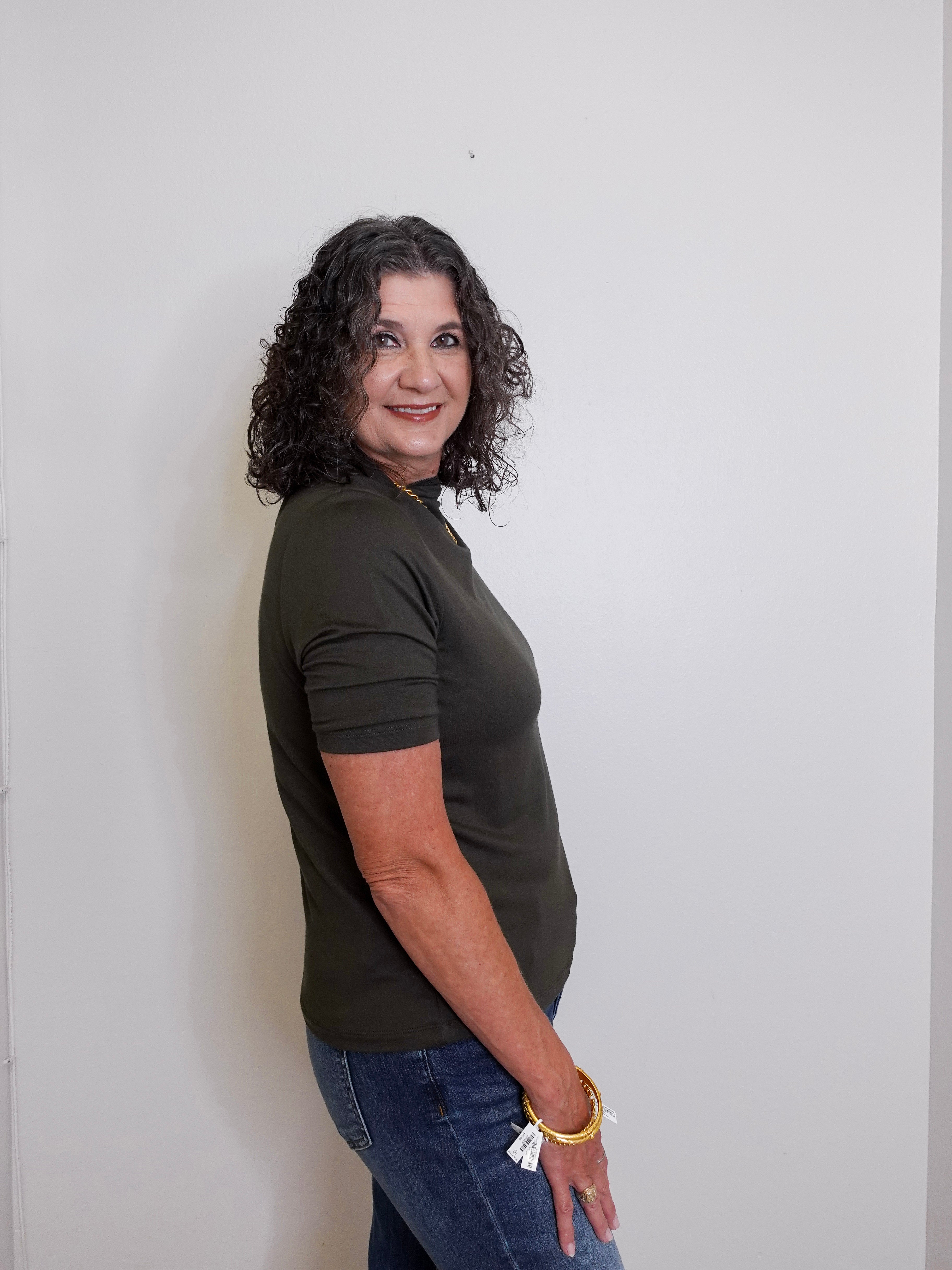 Woman wearing a green t-shirt and blue jeans against a white wall