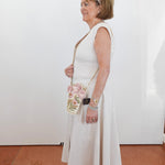 Woman in a white dress holding a floral handbag against a plain white wall.