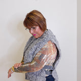 Woman wearing a gray fur vest over a gold sequin top against a white background