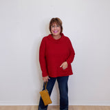 Woman wearing a red sweater and blue jeans, holding a yellow bag against a white background
