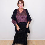 Woman wearing a black outfit with a patterned top against a white wall.