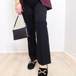 Person wearing black pants, maroon blazer, and black loafers with gold accents on a light wooden floor.