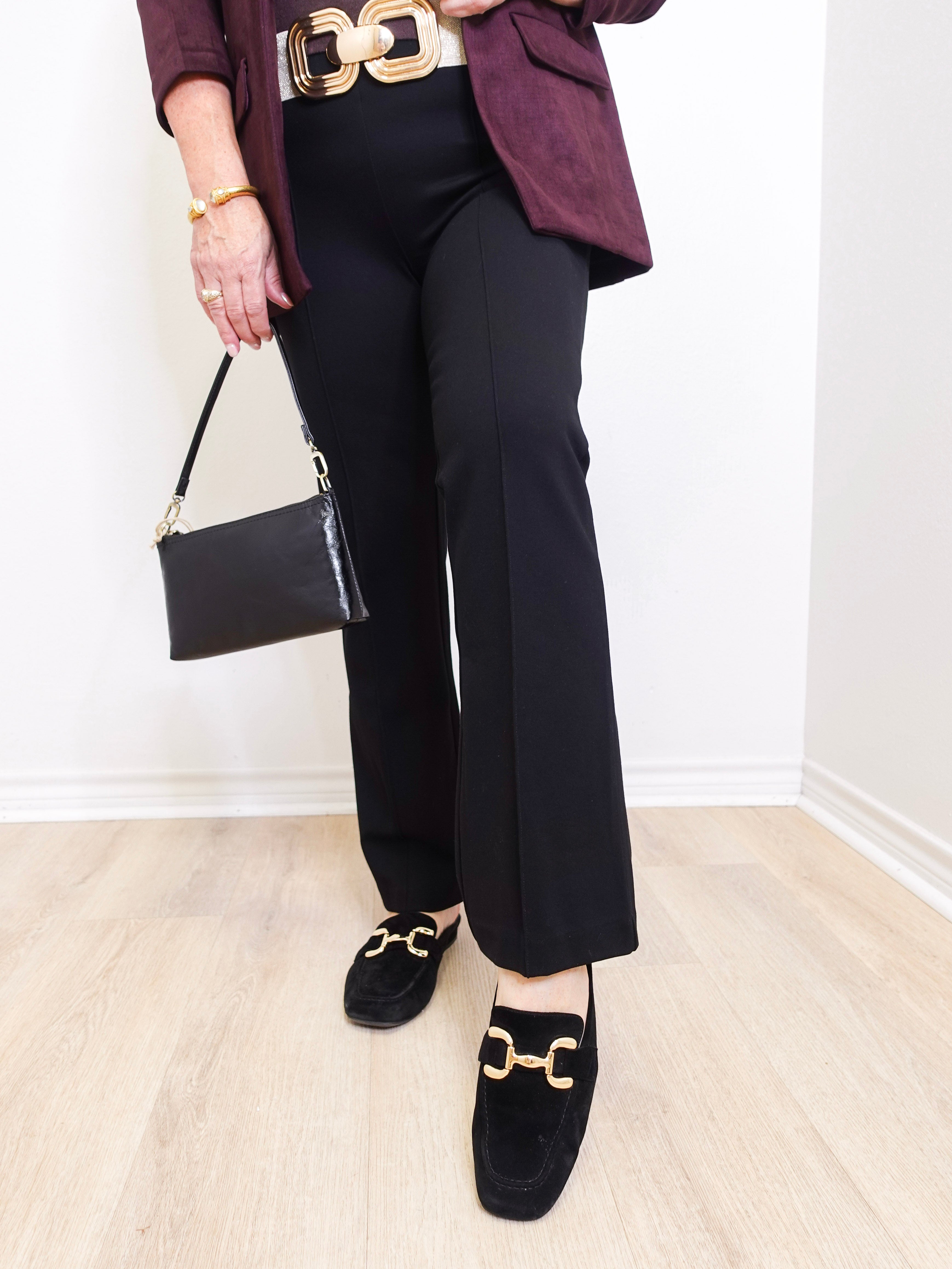 Person wearing black pants, maroon blazer, and black loafers with gold accents on a light wooden floor.