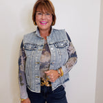 Woman wearing a denim jacket with floral patterns, holding a handbag against a white background