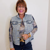 Woman wearing a denim jacket with floral patterns, holding a handbag against a white background