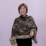 Woman wearing a leopard print poncho with fur trim against a light purple background