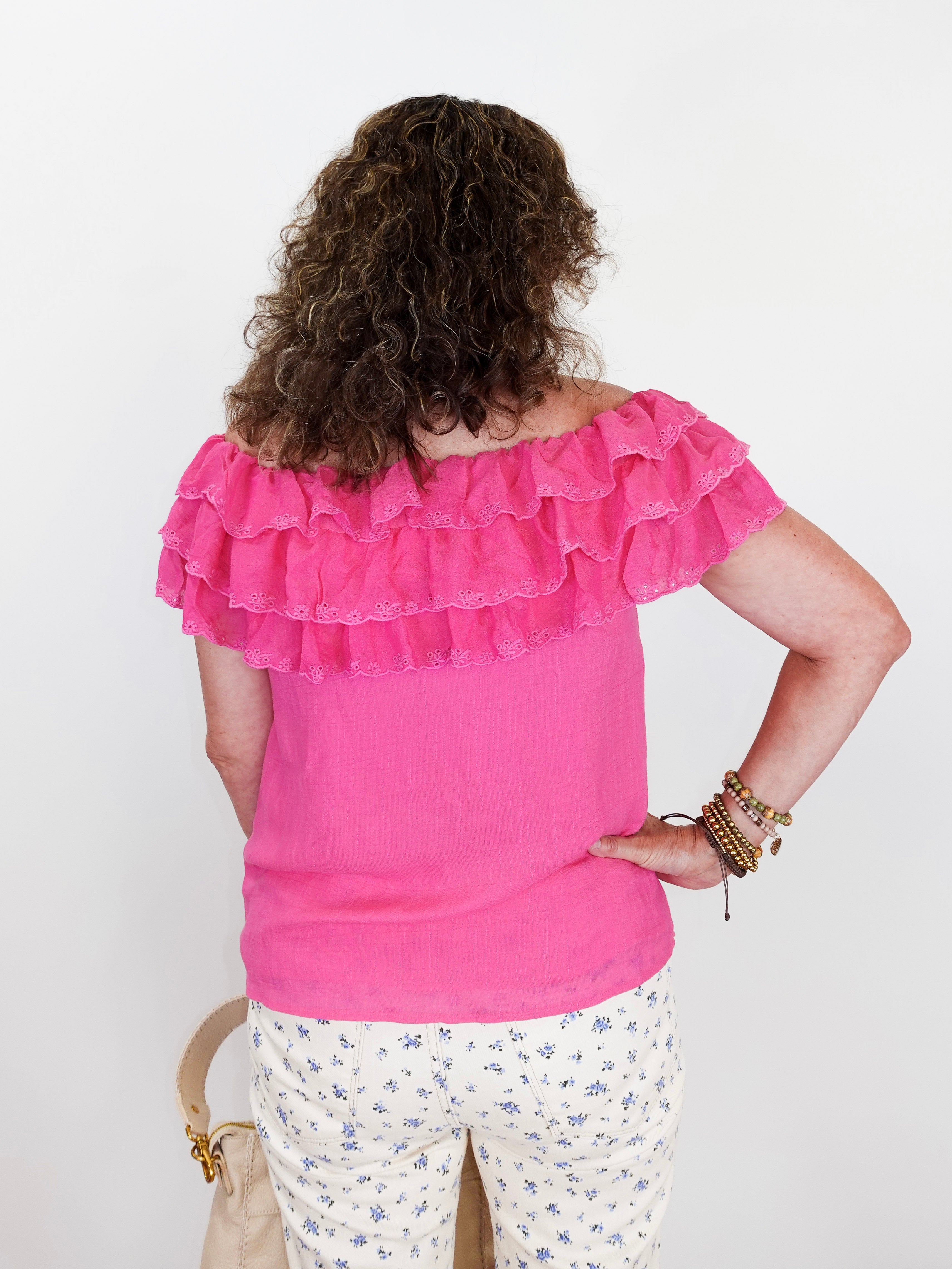 Person wearing a pink ruffled top and floral pants against a white background