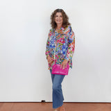 Woman wearing a colorful floral blouse and blue jeans, holding a pink bag against a white background.