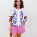 Woman wearing a colorful shirt with floral patterns and pink shorts against a white background