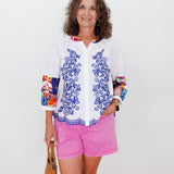 Woman wearing a colorful shirt with floral patterns and pink shorts against a white background