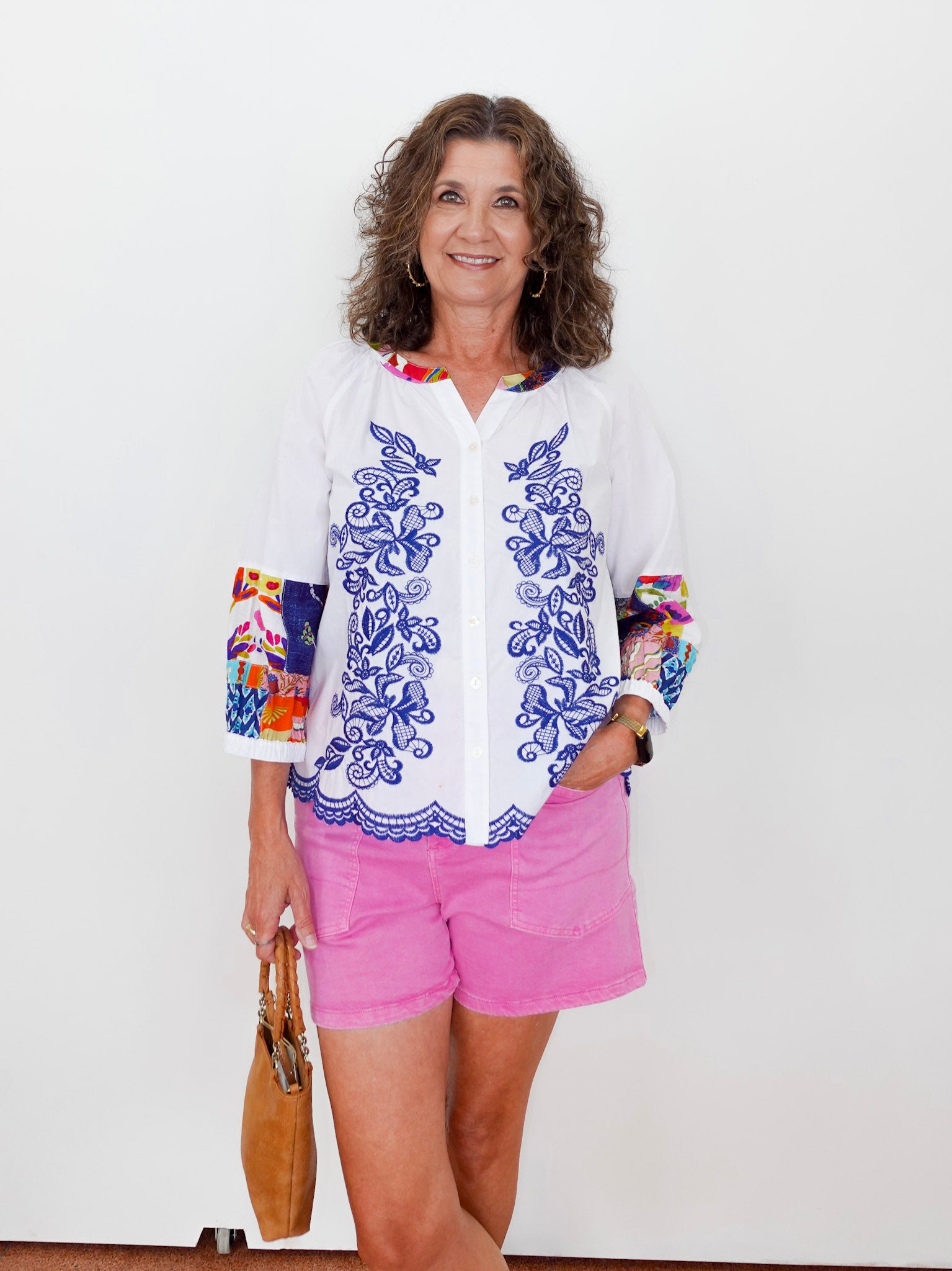 Woman wearing a colorful shirt with floral patterns and pink shorts against a white background