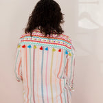 Person wearing a colorful striped shirt with pom-pom details on a plain background