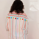 Person wearing a colorful striped shirt with pom-pom details on a plain background