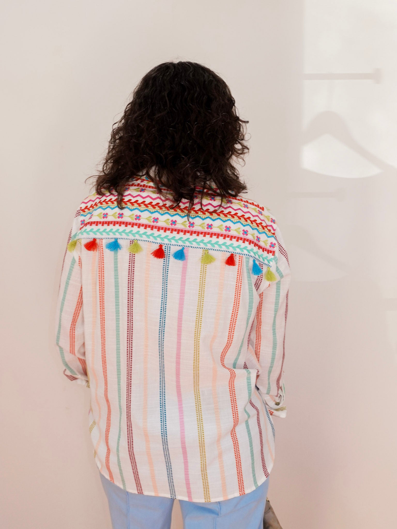 Person wearing a colorful striped shirt with pom-pom details on a plain background