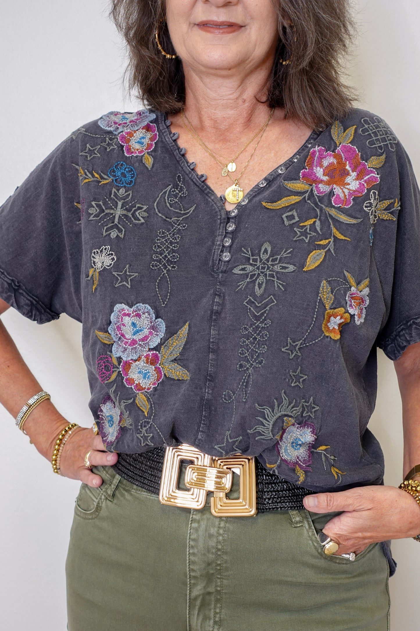 Woman wearing a dark gray blouse with floral and geometric embroidery, standing against a plain background.
