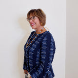 Woman wearing a navy patterned blouse against a white wall