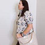 Woman holding a beige handbag against a white wall