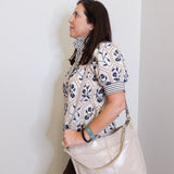 Woman holding a beige handbag against a white wall