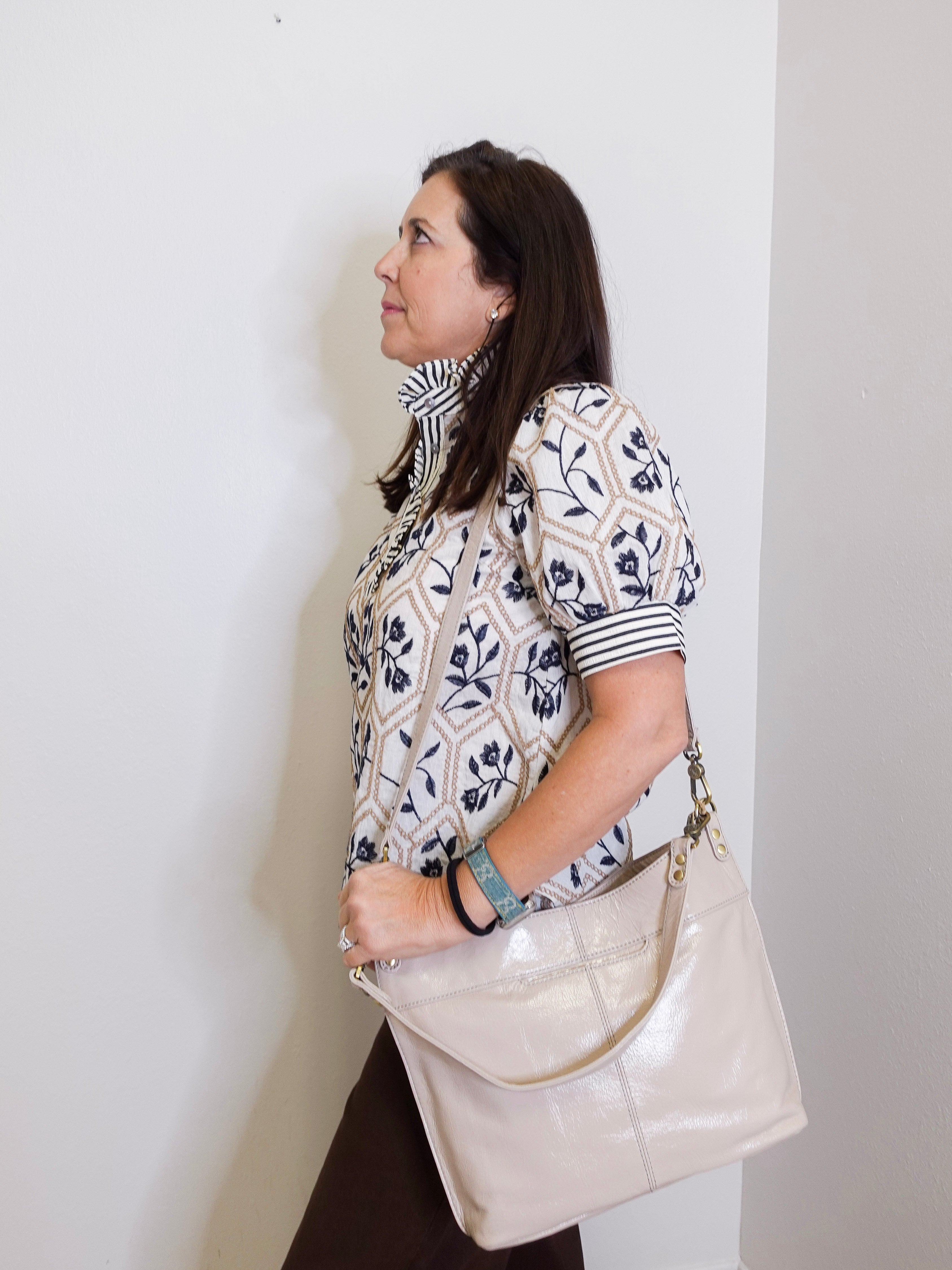 Woman holding a beige handbag against a white wall