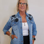Woman wearing a denim jacket with floral embroidery on a plain background