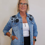 Woman wearing a denim jacket with floral embroidery on a plain background