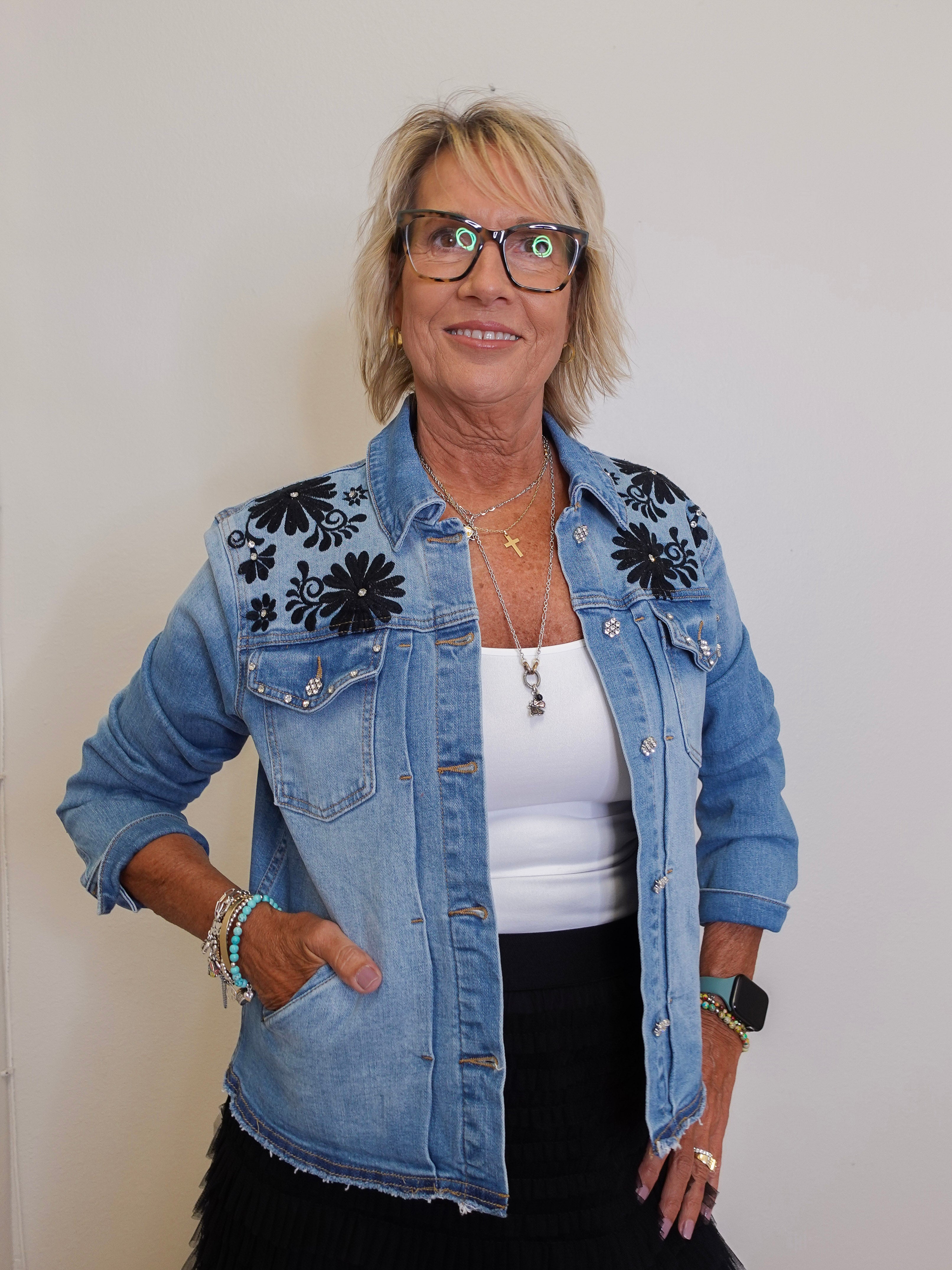 Woman wearing a denim jacket with floral embroidery on a plain background
