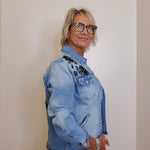 Person wearing a light blue denim jacket with floral embroidery on a plain background