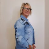 Person wearing a light blue denim jacket with floral embroidery on a plain background