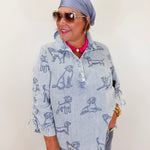 Woman wearing a light blue shirt with dog print, sunglasses, and headscarf against a plain background