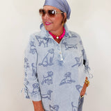 Woman wearing a light blue shirt with dog print, sunglasses, and headscarf against a plain background