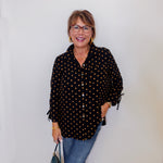 Woman wearing a black polka dot blouse and blue jeans against a white wall