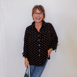 Woman wearing a black polka dot blouse and blue jeans against a white wall