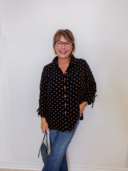 Woman wearing a black polka dot blouse and blue jeans against a white wall
