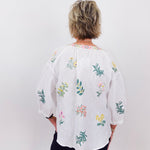 Person wearing a white blouse with colorful floral embroidery against a white background