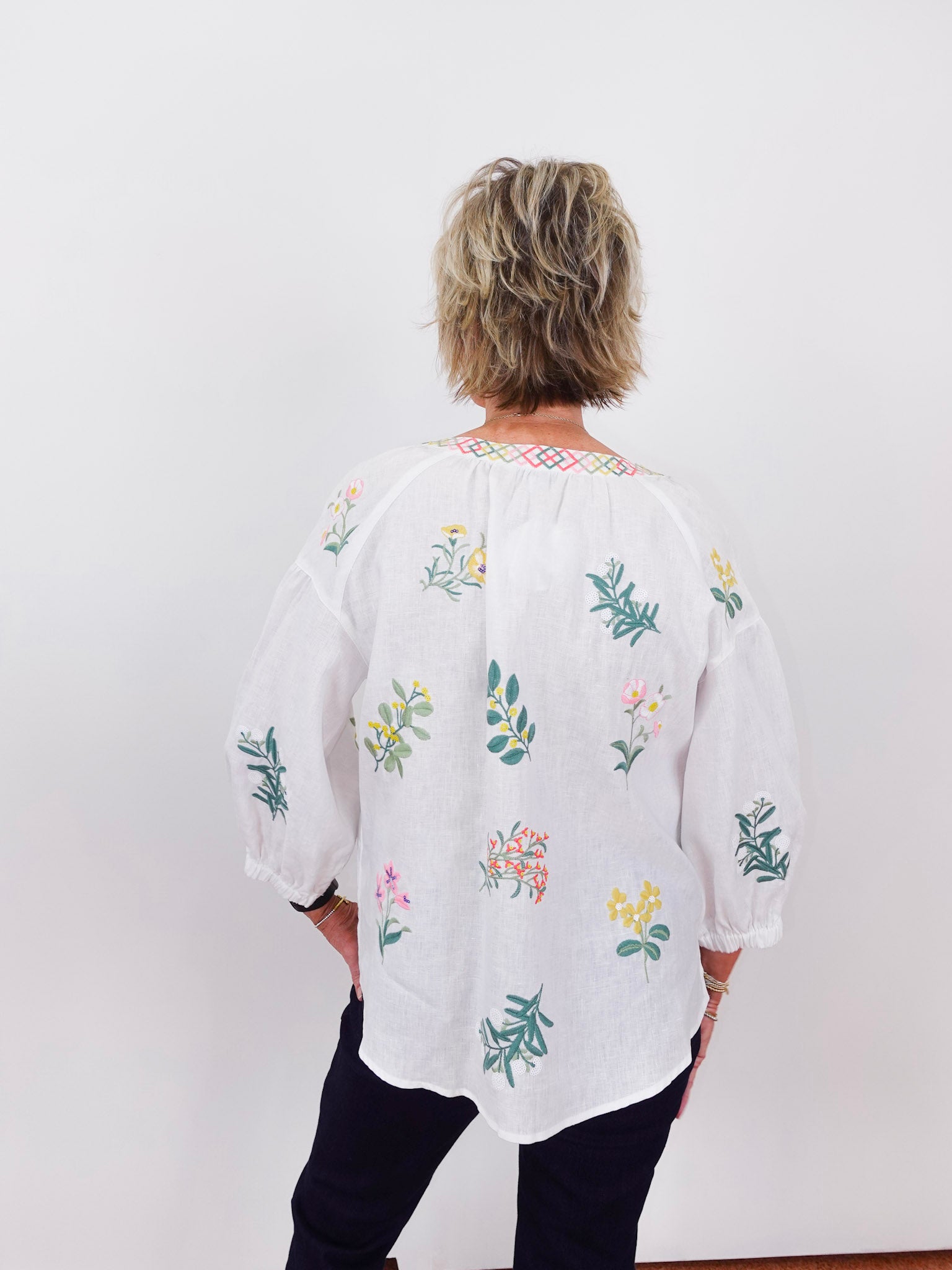 Person wearing a white blouse with colorful floral embroidery against a white background