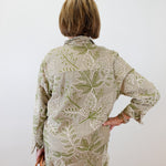 Person wearing a green and beige floral outfit against a white wall.