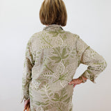 Person wearing a green and beige floral outfit against a white wall.