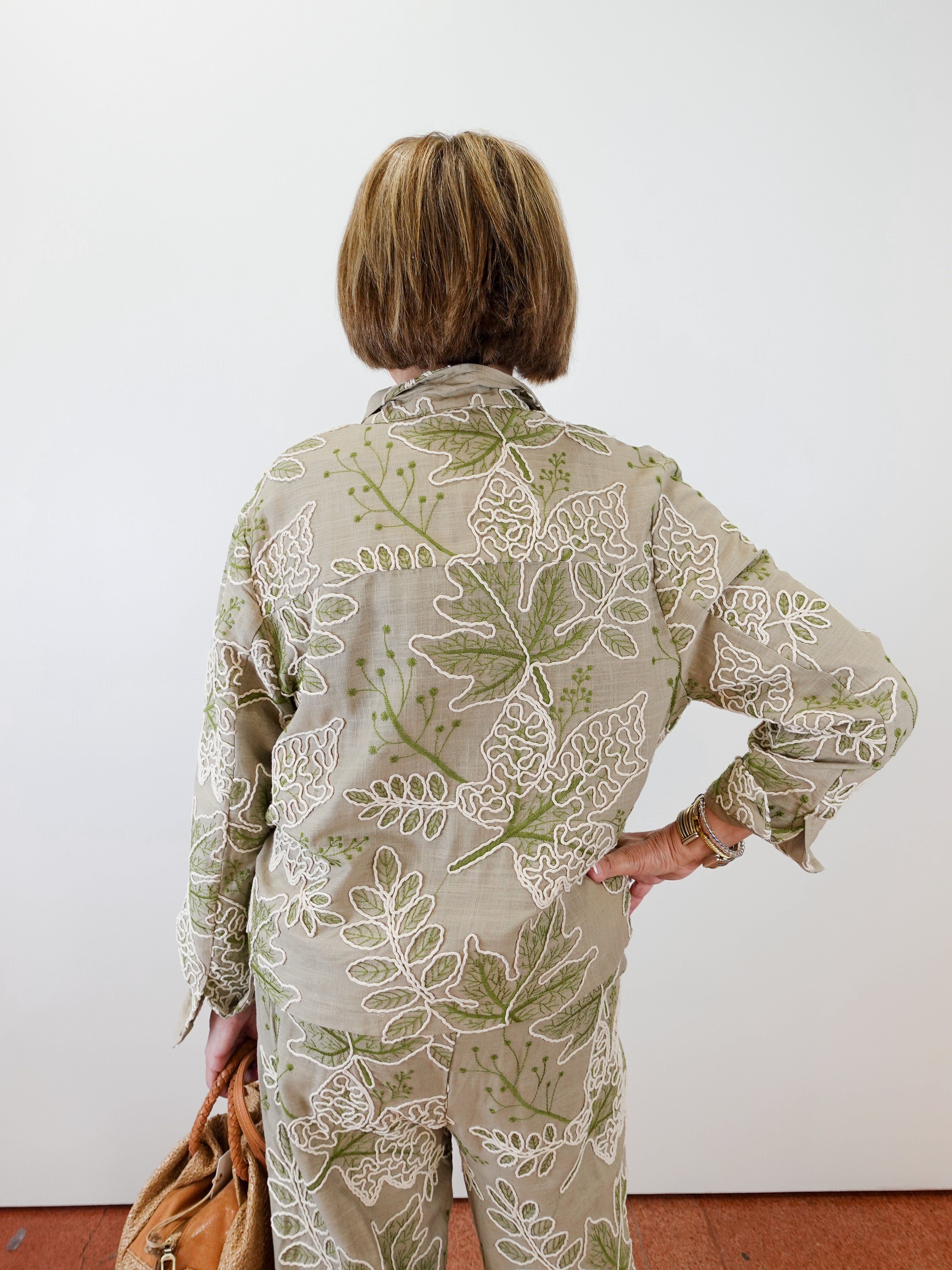 Person wearing a green and beige floral outfit against a white wall.