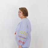 Woman wearing a light blue blouse with colorful embroidery on a white background
