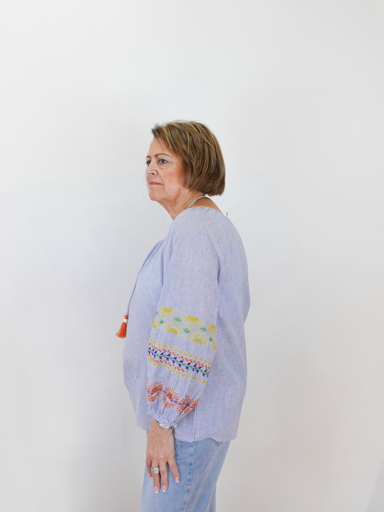 Woman wearing a light blue blouse with colorful embroidery on a white background