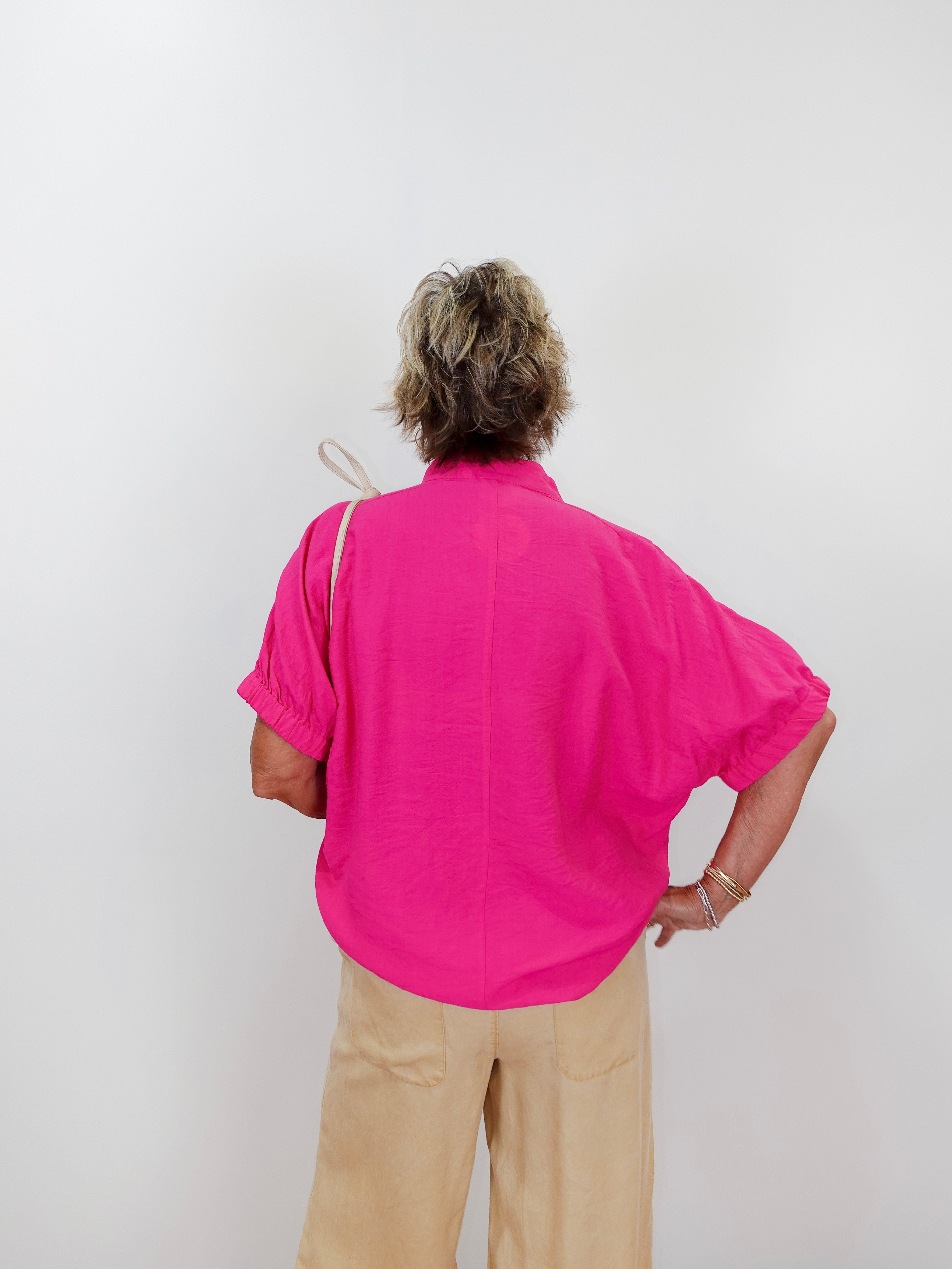 Person wearing a bright pink shirt and beige pants against a white background